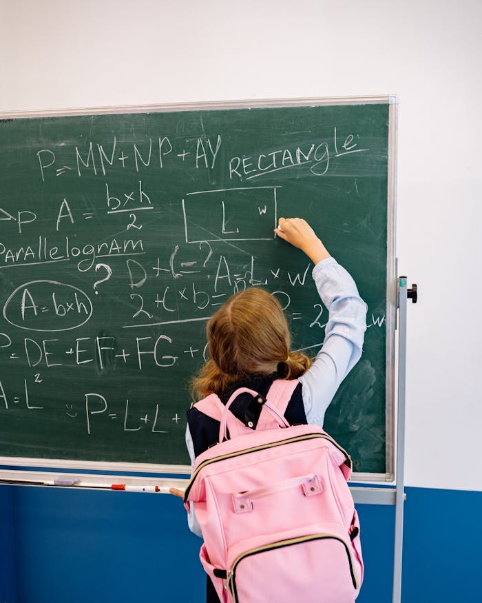 About Young student writing math formulas on a blackboard in a classroom, focused on learning.